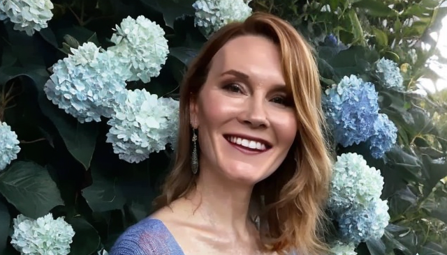 Dr. Deirdre Conroy smiling in front of flower bush with blue flowers blooming.